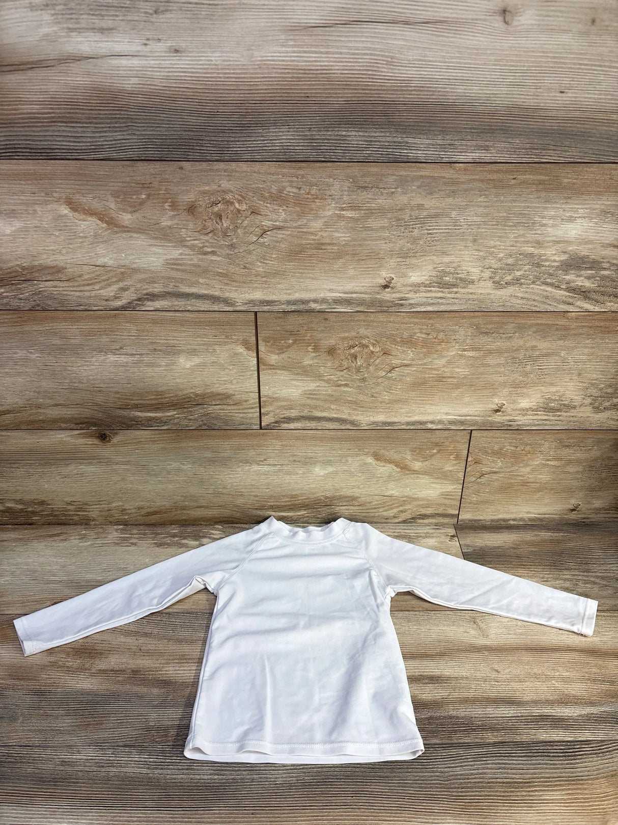 Flat lay of white long-sleeve UPF 50 toddler rash guard (2T) showing front and full sleeves on wood plank background