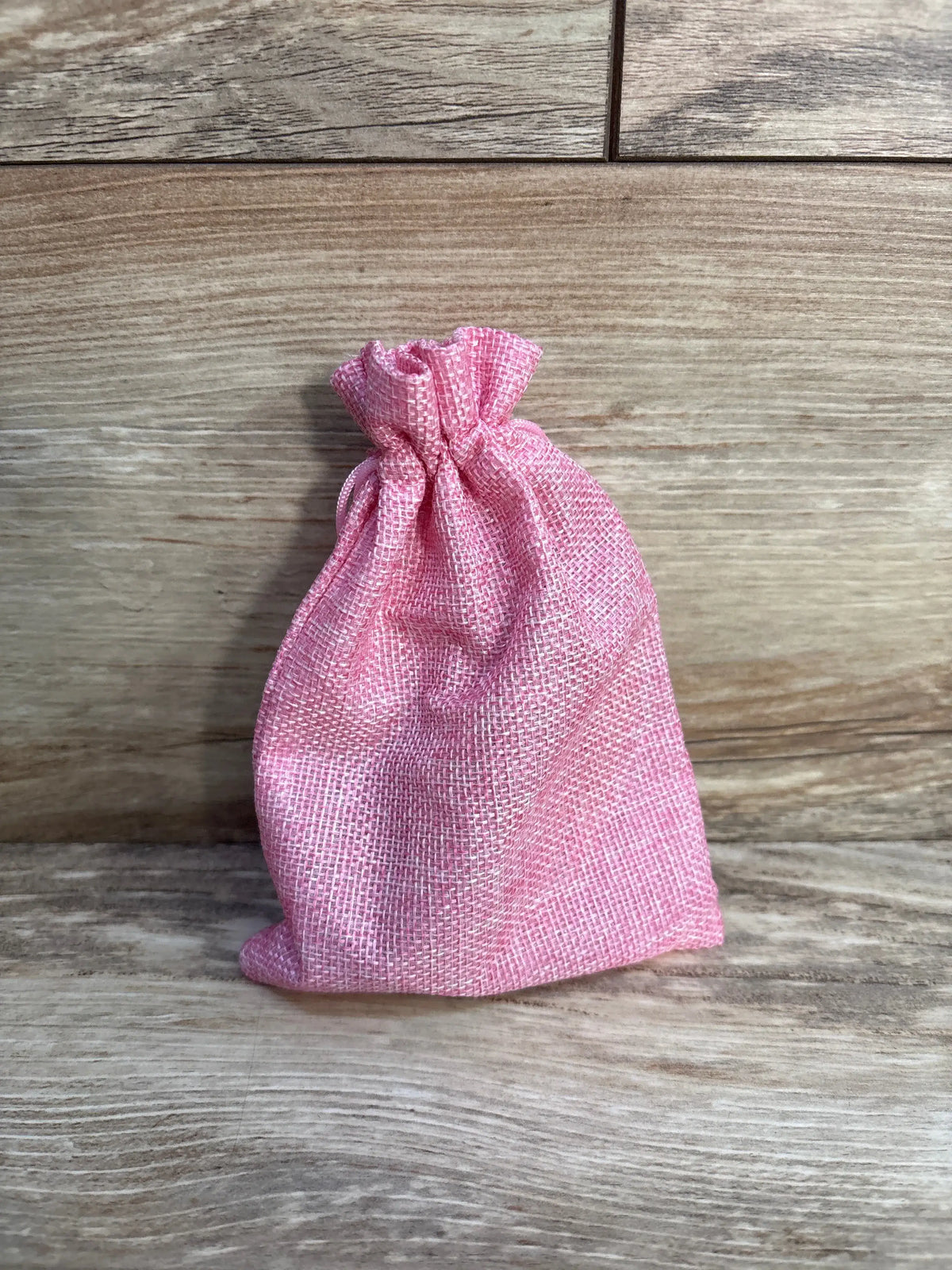 Front view of FSYQUAST 2pc Birth Comb and Acupressure Massage Ball Set storage bag with pink drawstring on wood grain