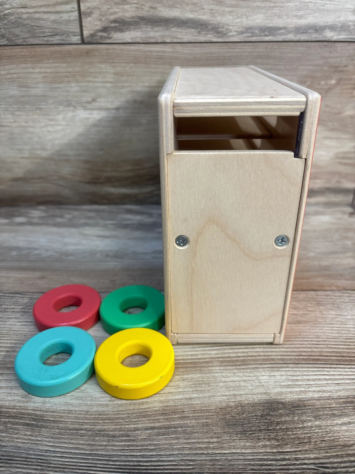 Side view of Lovevery Count & Slide Ring Chute showing natural plywood chute and four colored wooden rings on a wood surface
