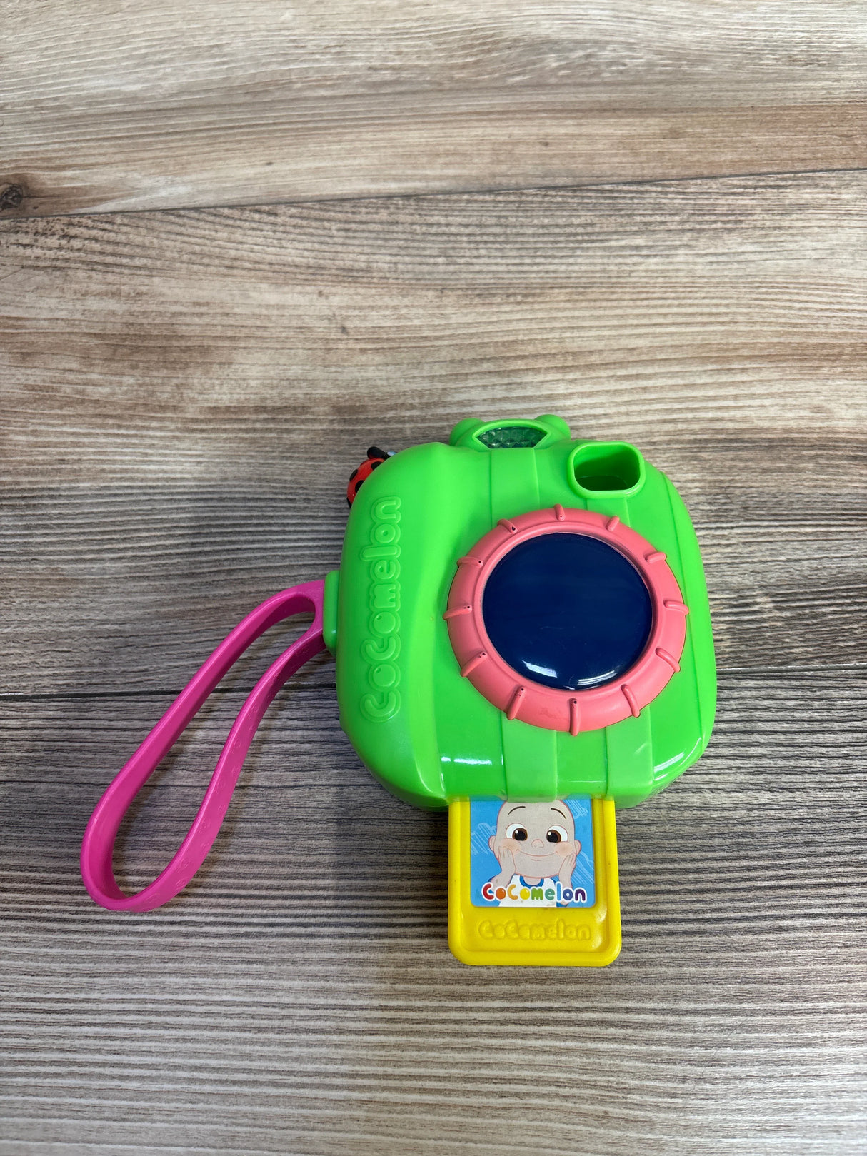 Green CoComelon toy camera with pink strap and character image on wooden surface