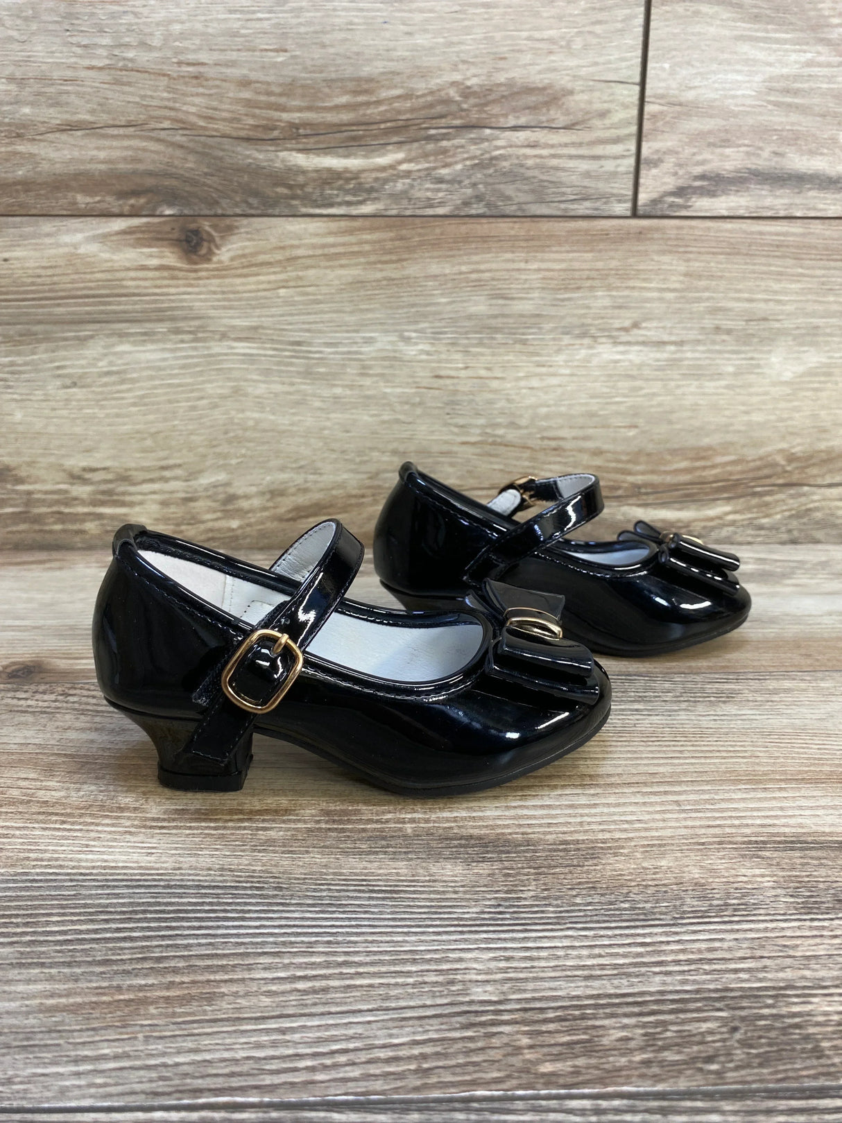 Girls black patent leather dress shoes with bows and buckle straps on wood background
