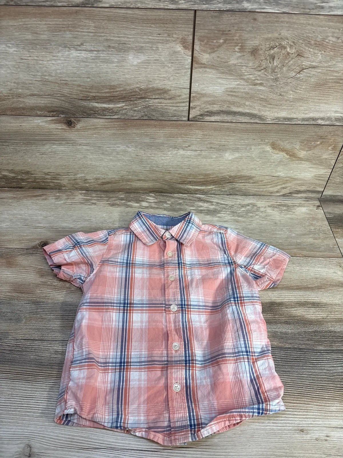Flat lay of pink Oshkosh short-sleeve button-up shirt 4T showing plaid pattern and white buttons on wood floor background
