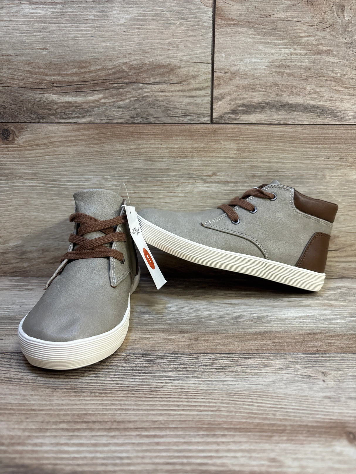 Kids taupe high-top sneakers with brown laces and white soles on wood floor