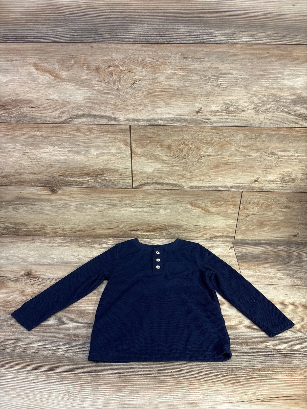 Flat lay of Cat & Jack navy waffle knit henley shirt, toddler size 3T, showcasing three-button placket, chest pocket and long sleeves on light wood background