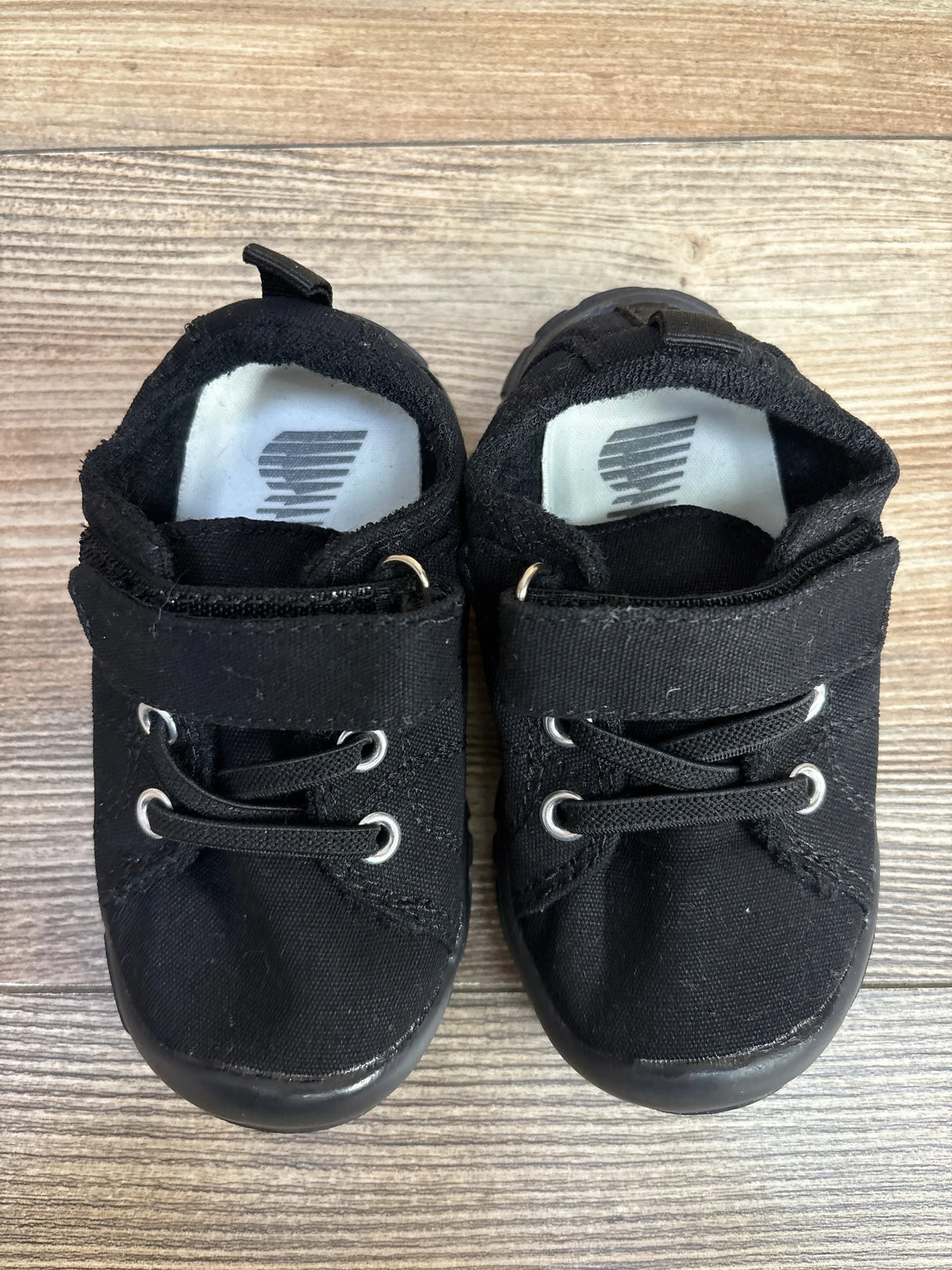 Pair of black baby shoes with canvas material and lace-up design on wooden floor