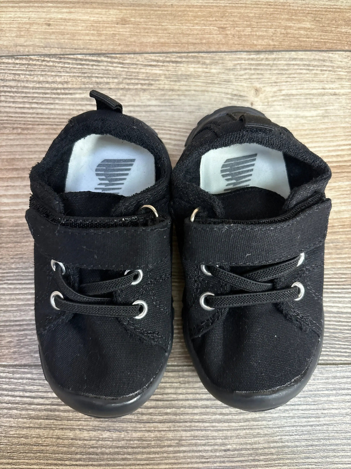 Pair of black baby shoes with canvas material and lace-up design on wooden floor