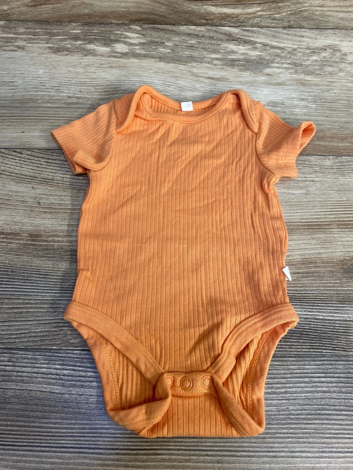 Top view of orange Mori ribbed bodysuit 0-3M showing lap-shoulder neckline, short sleeves and three-snap crotch on wood