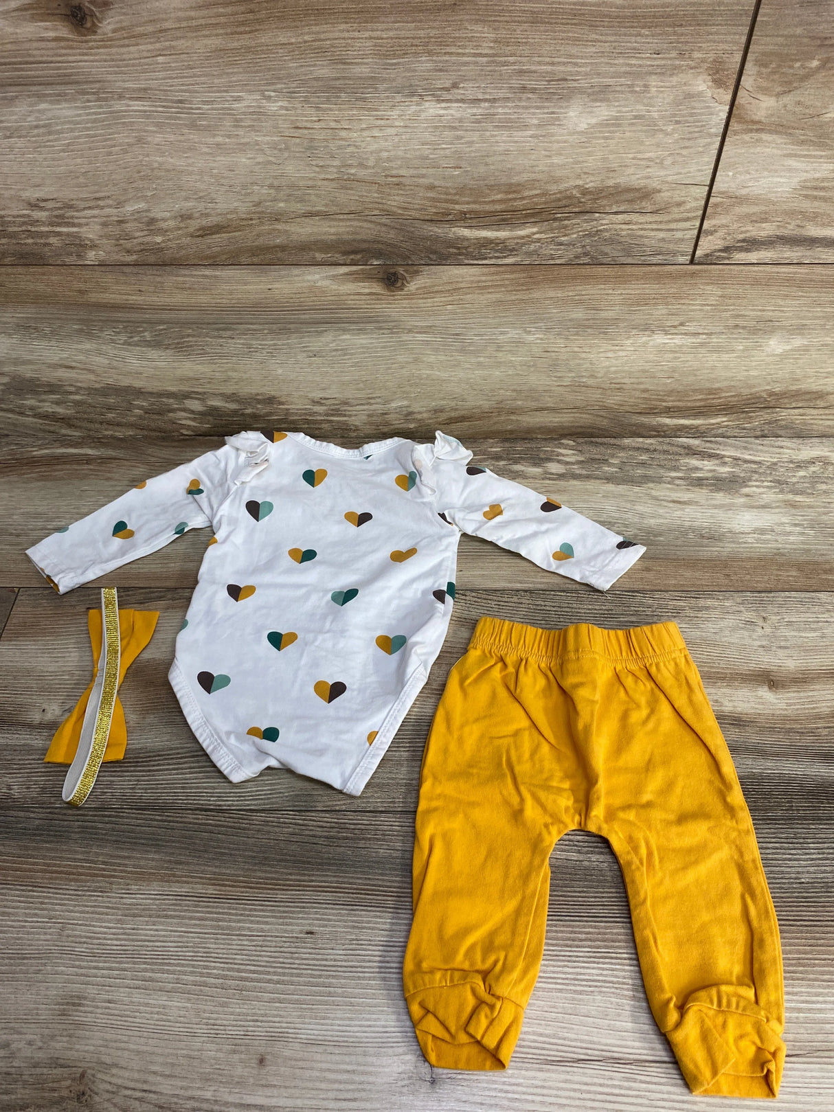 Baby outfit set on wood floor with heart print white bodysuit, yellow pants and matching headband