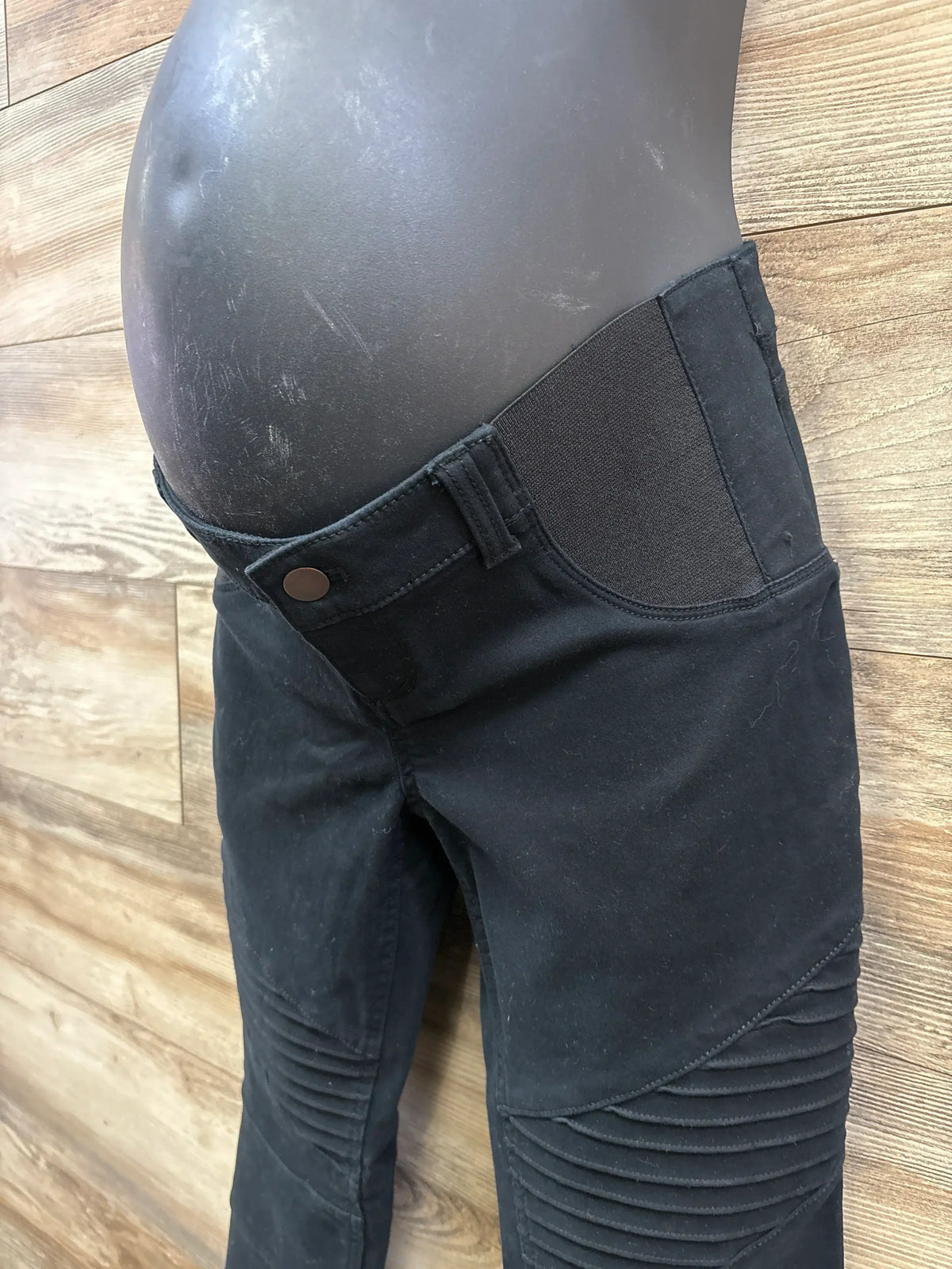 Black maternity pants with stretch side panels on a mannequin, wood floor background