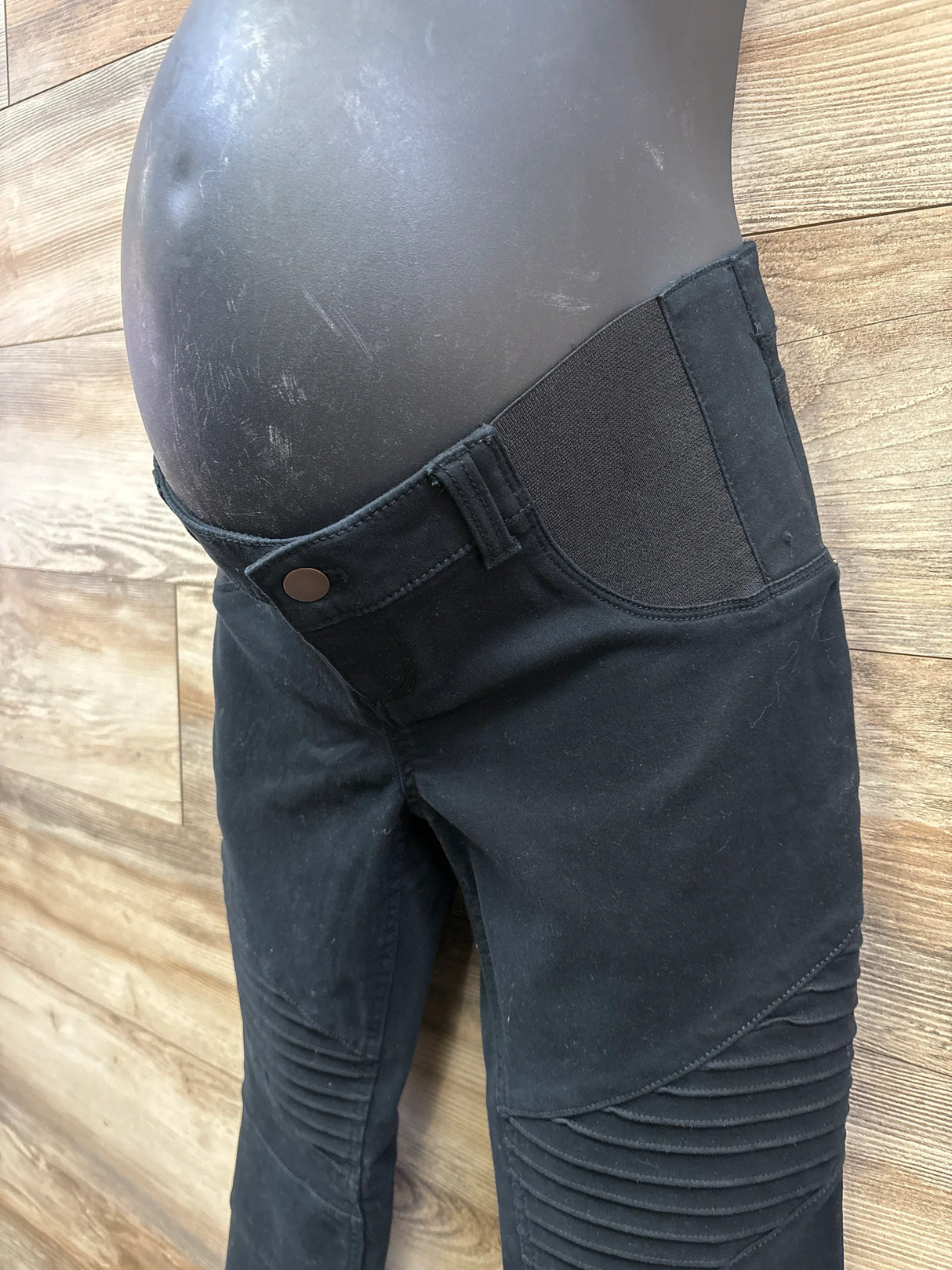 Black maternity pants with stretch side panels on a mannequin, wood floor background