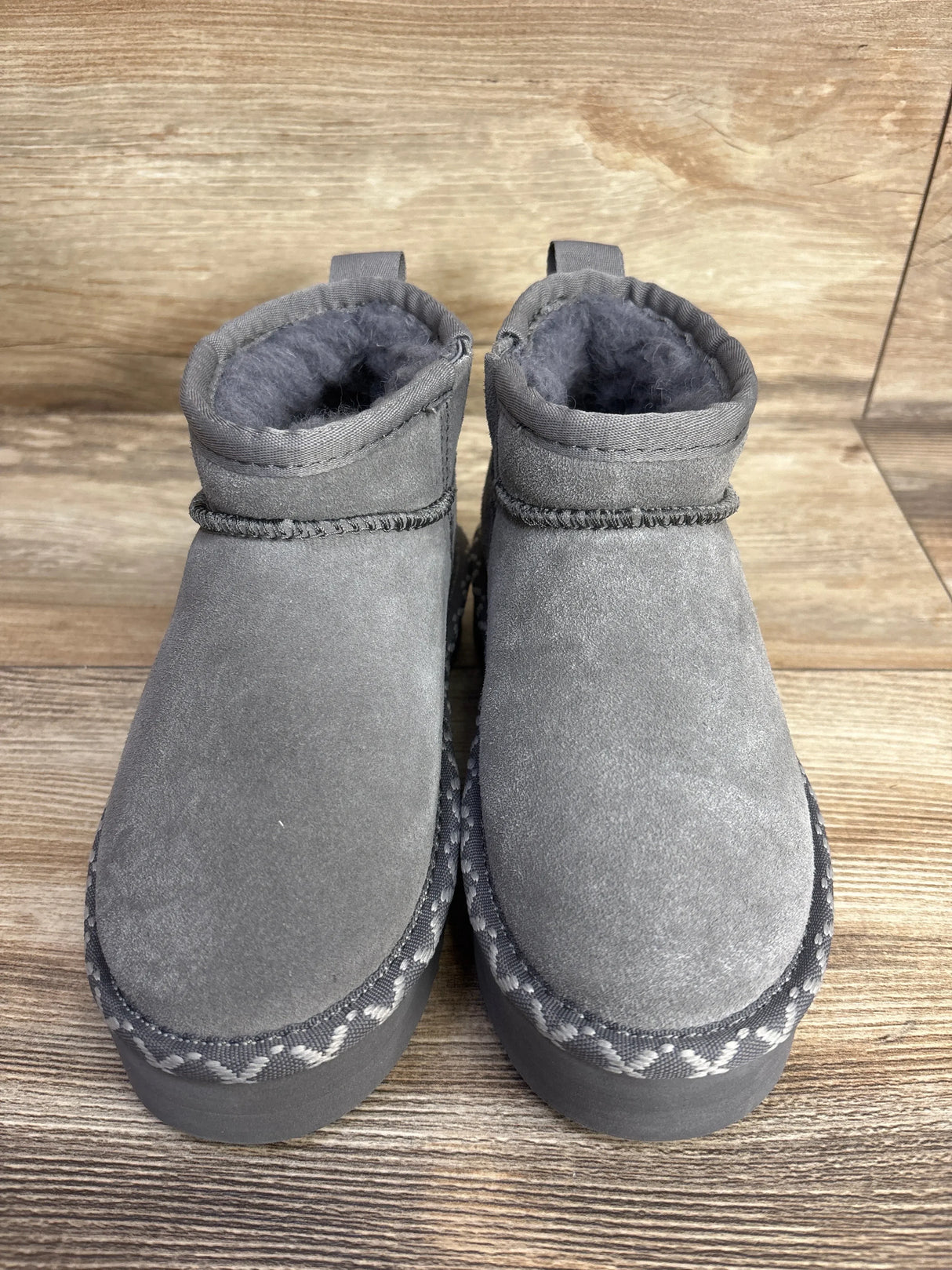 Gray suede kids winter boots with plush lining and textured soles on wood background