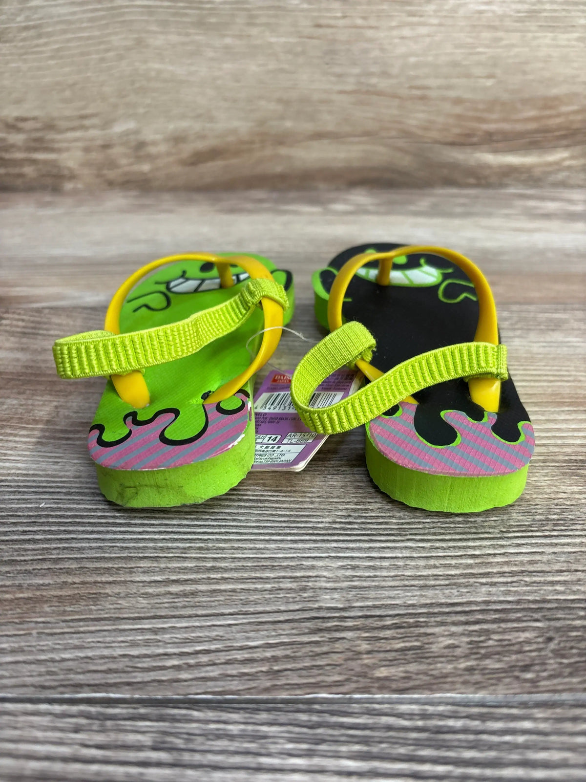 Front view of toddler lime and black character flip-flops with neon yellow straps and adjustable heel loop on wood background