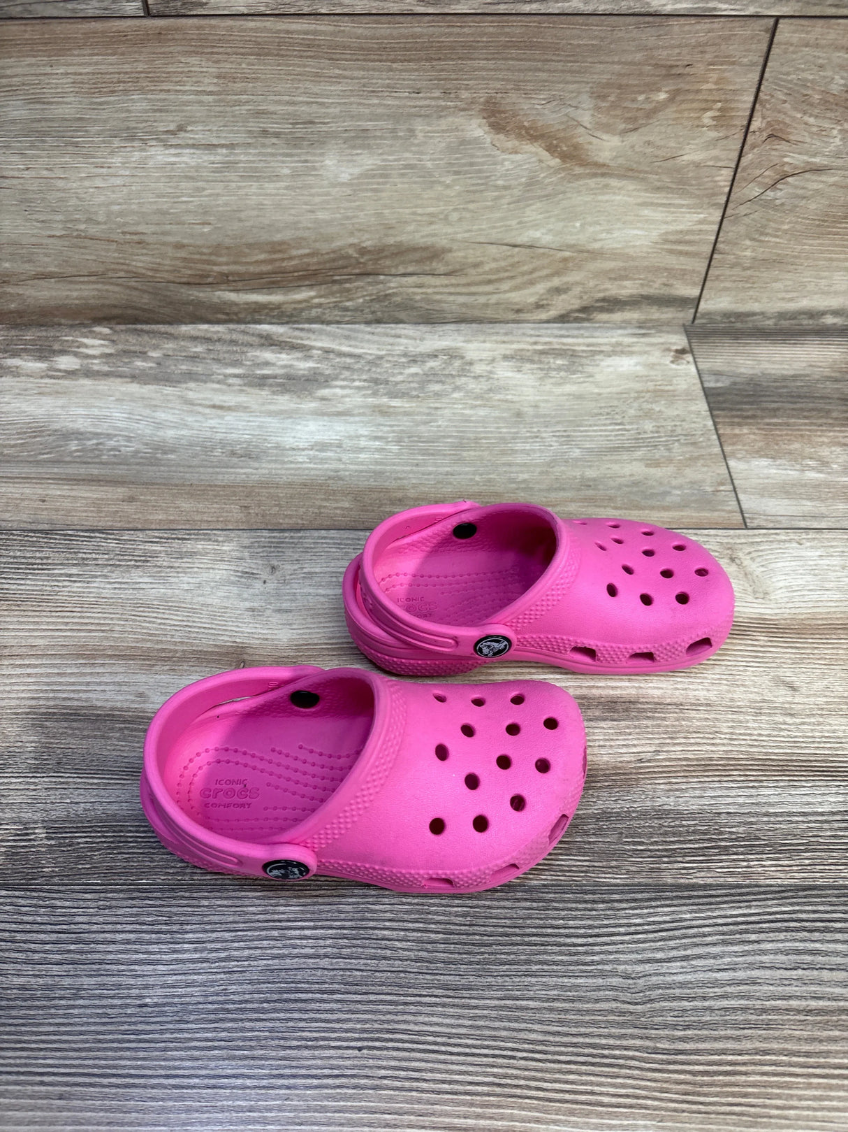 Top-down view of pair of pink Crocs Classic clogs showcasing ventilation holes and heel straps with wood-look floor background
