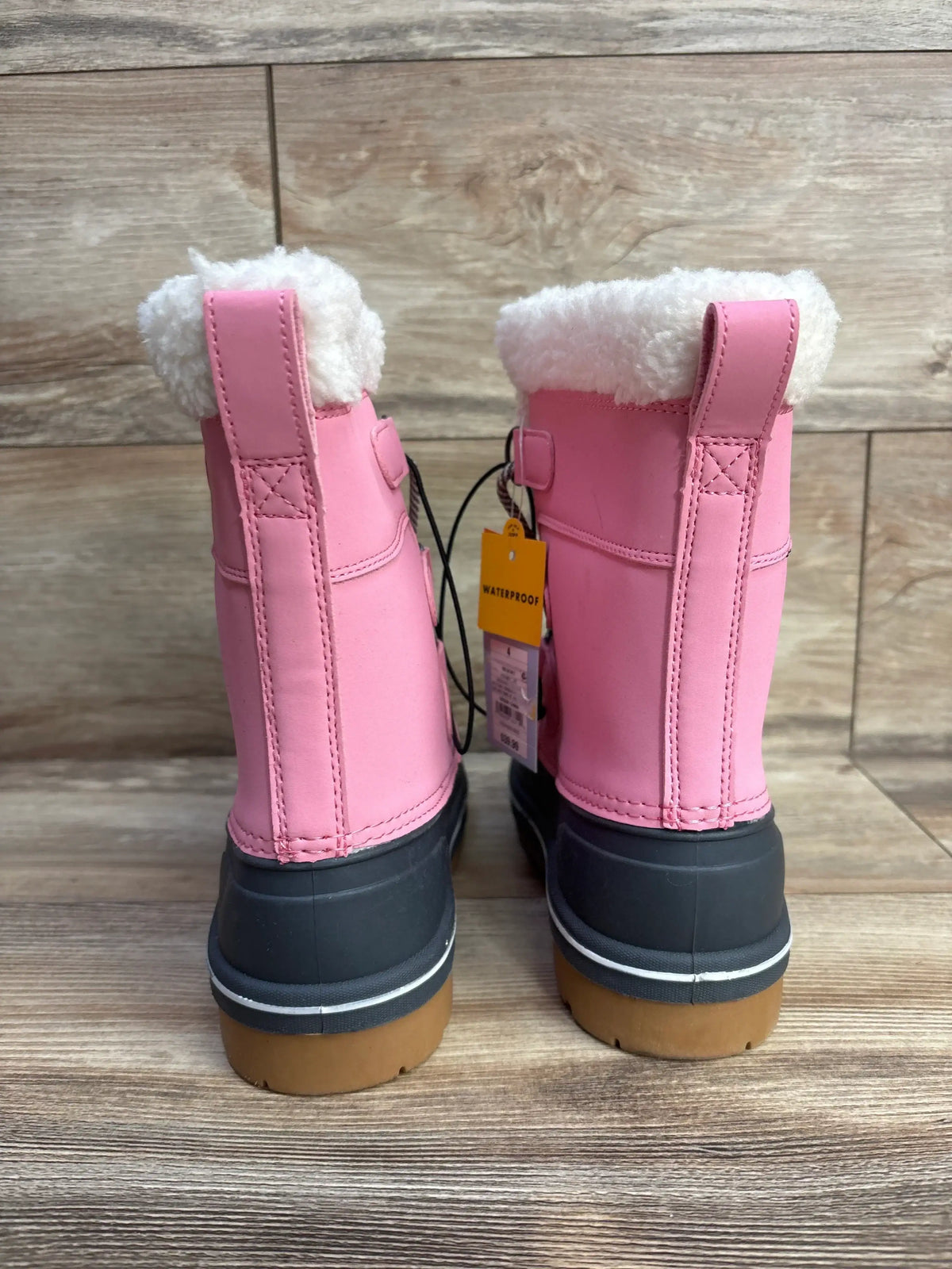 Pink waterproof kids winter boots with faux fur lining on wooden floor