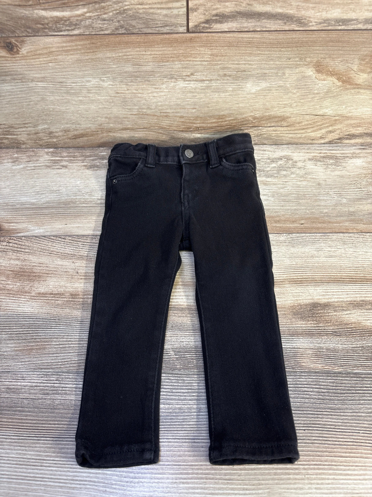 Top down view of black Cat and Jack toddler jeggings showing front button, belt loops and straight legs on a light wood background