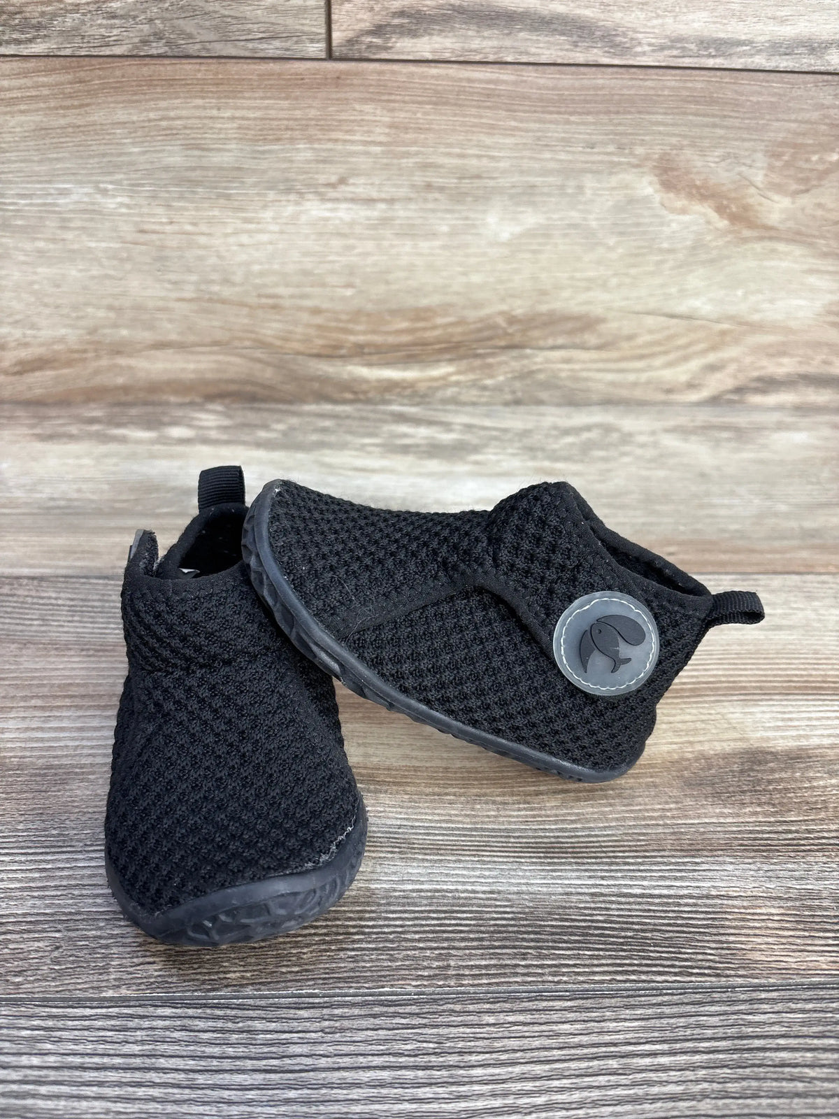 Angled view of black FEETCITY high-top mesh sock shoes showcasing textured mesh uppers and pull tabs on wood-grain background
