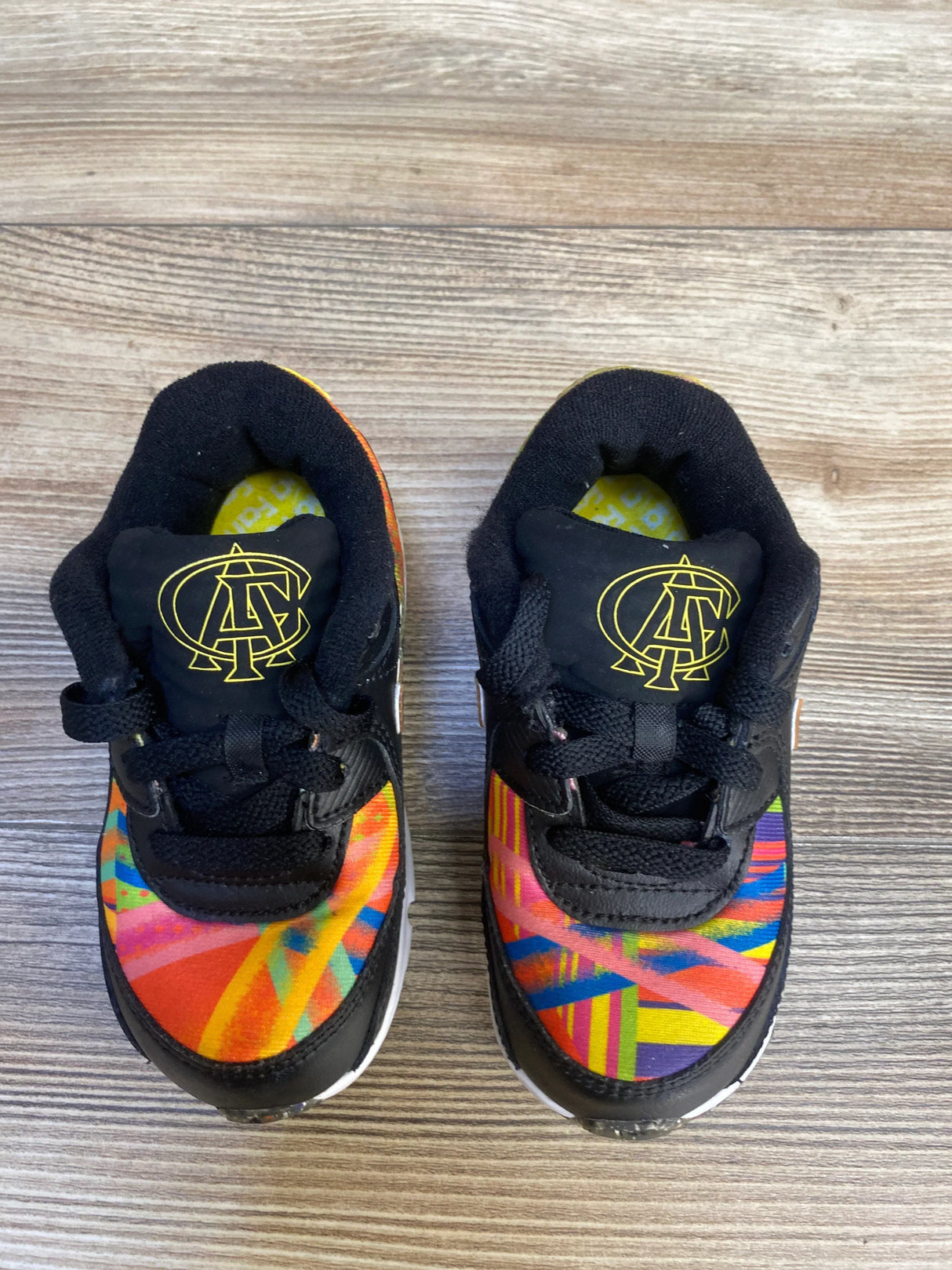 Colorful toddler sneakers with geometric patterns and black laces on wood floor