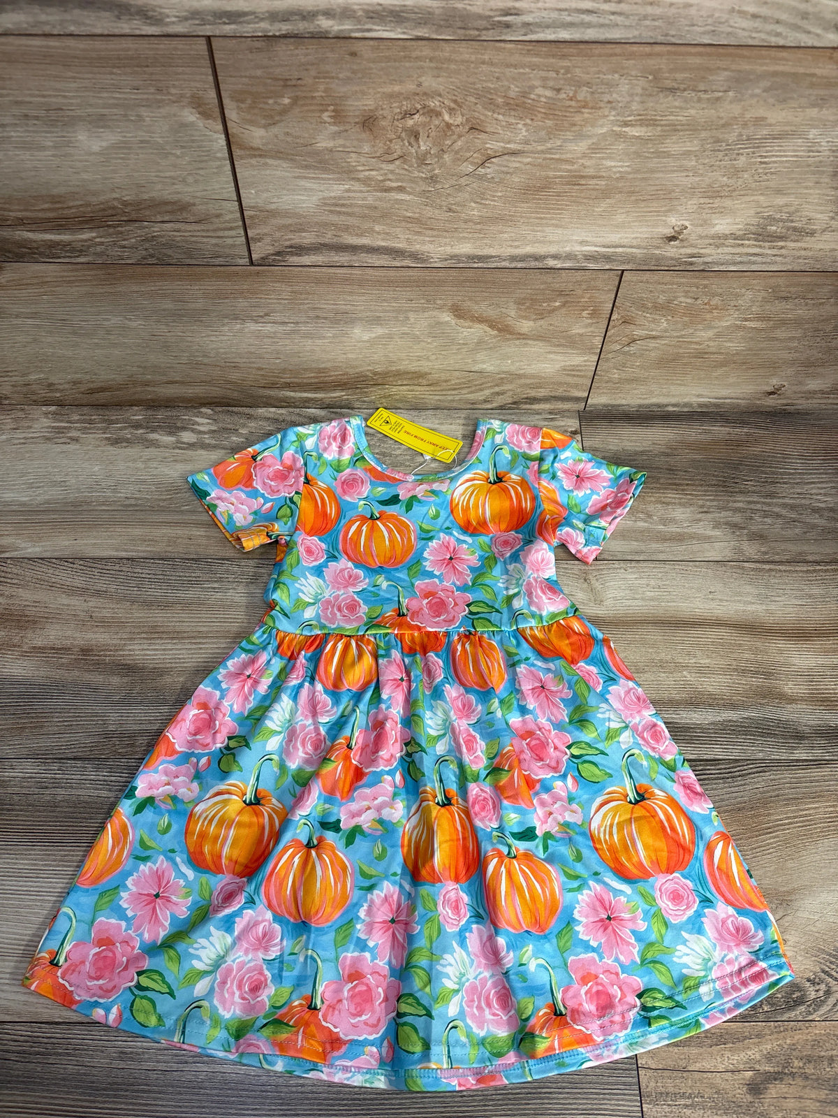 Colorful toddler dress with orange pumpkin and pink flower pattern on wood floor