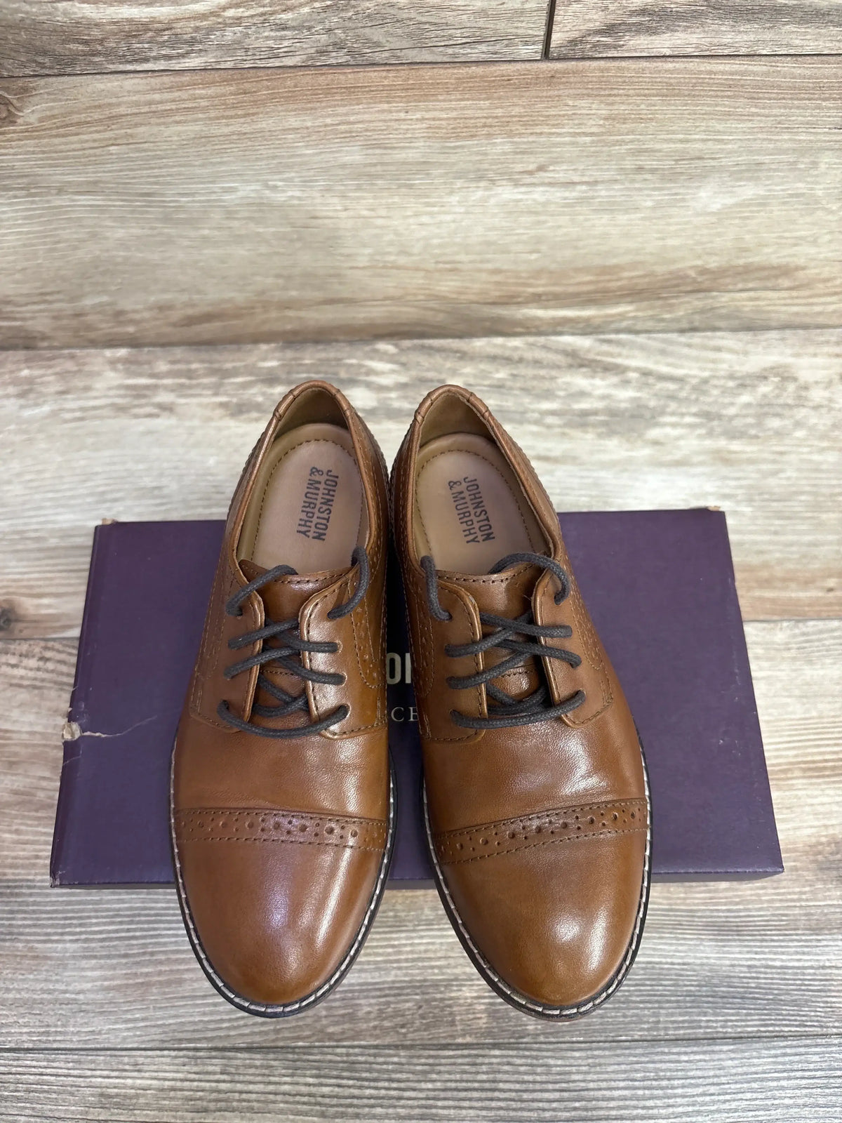 Pair of brown leather Johnston & Murphy dress shoes with black laces on a purple box, wooden background
