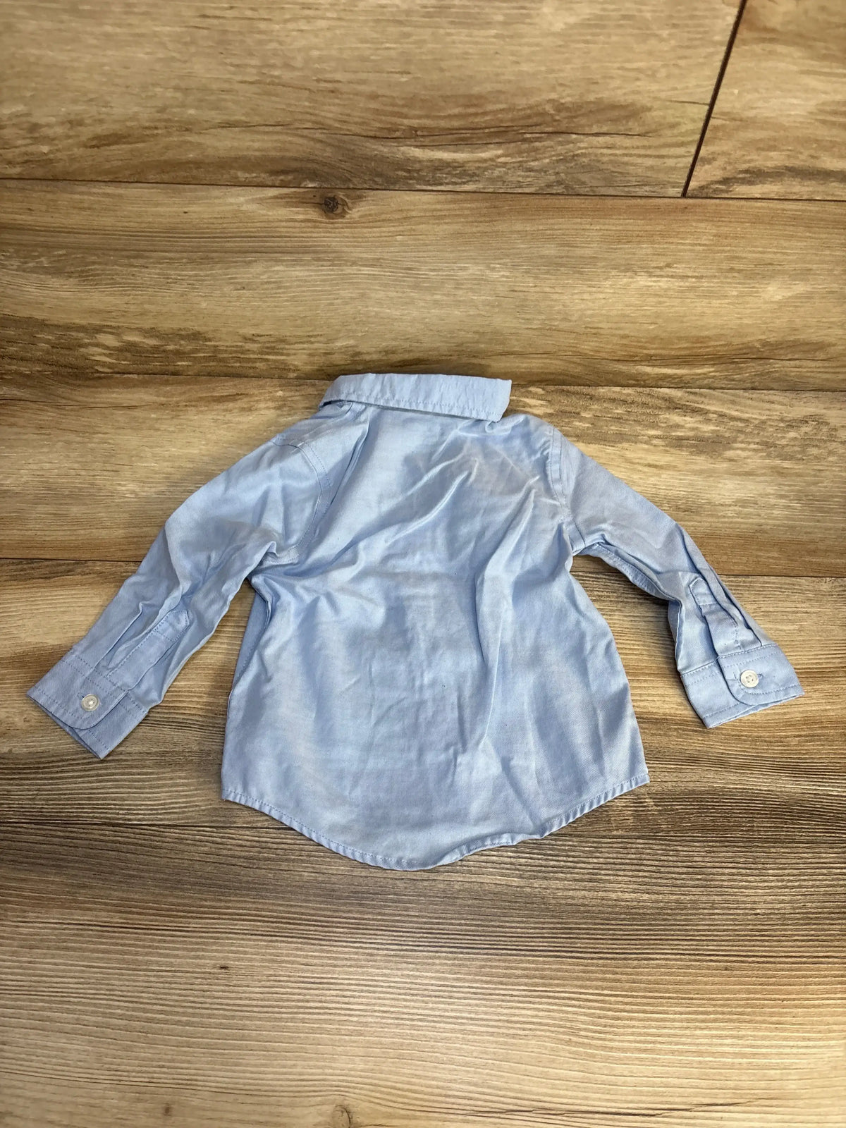 Light blue long sleeve button-up toddler shirt on wood floor, gently used kids clothing