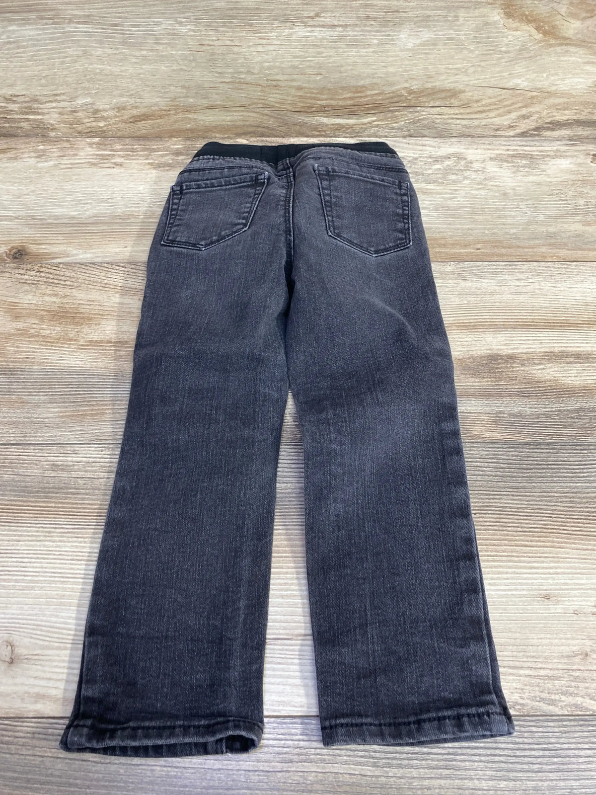 Children's black denim jeans with pockets, laid flat on wooden background