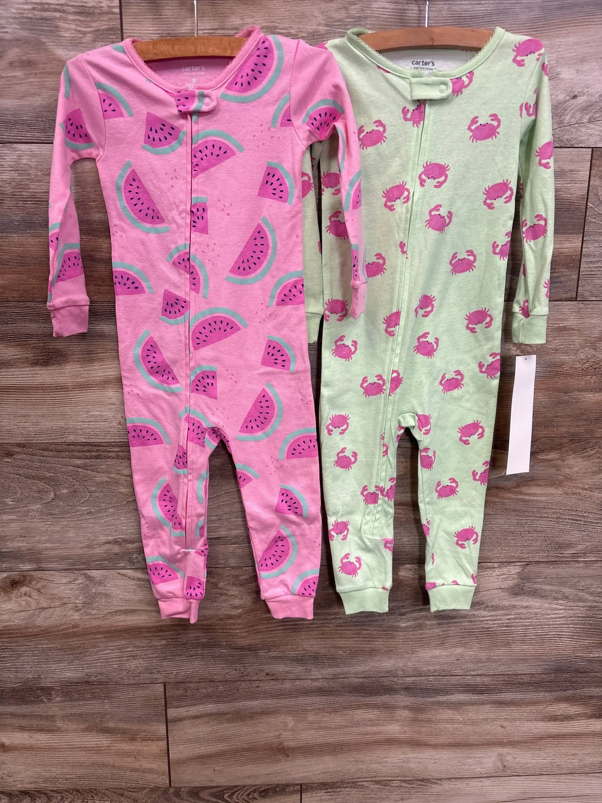 Front view of 2-pack baby sleeper set showing pink watermelon and green crab prints, long sleeves and front zippers on wood background