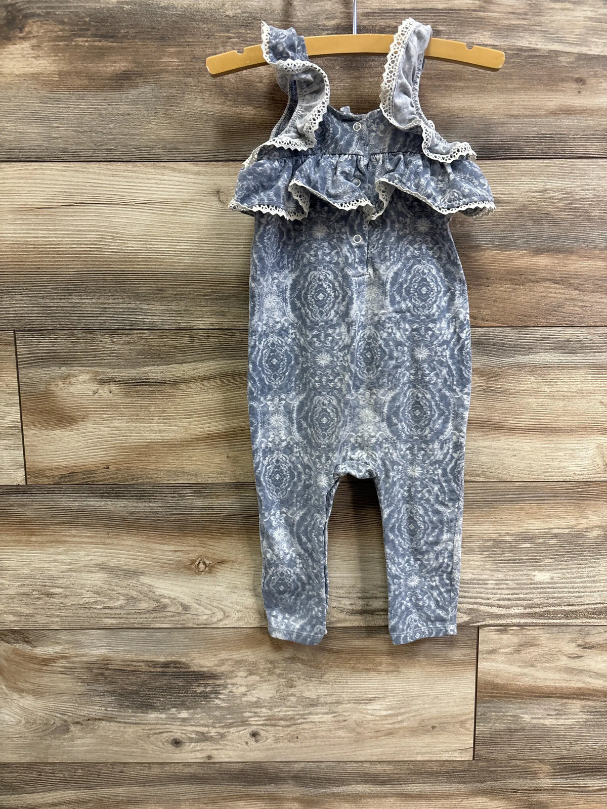 Front view of Jessica Simpson floral jumpsuit showcasing blue floral fabric, lace-trimmed ruffles and snaps on a wooden hanger