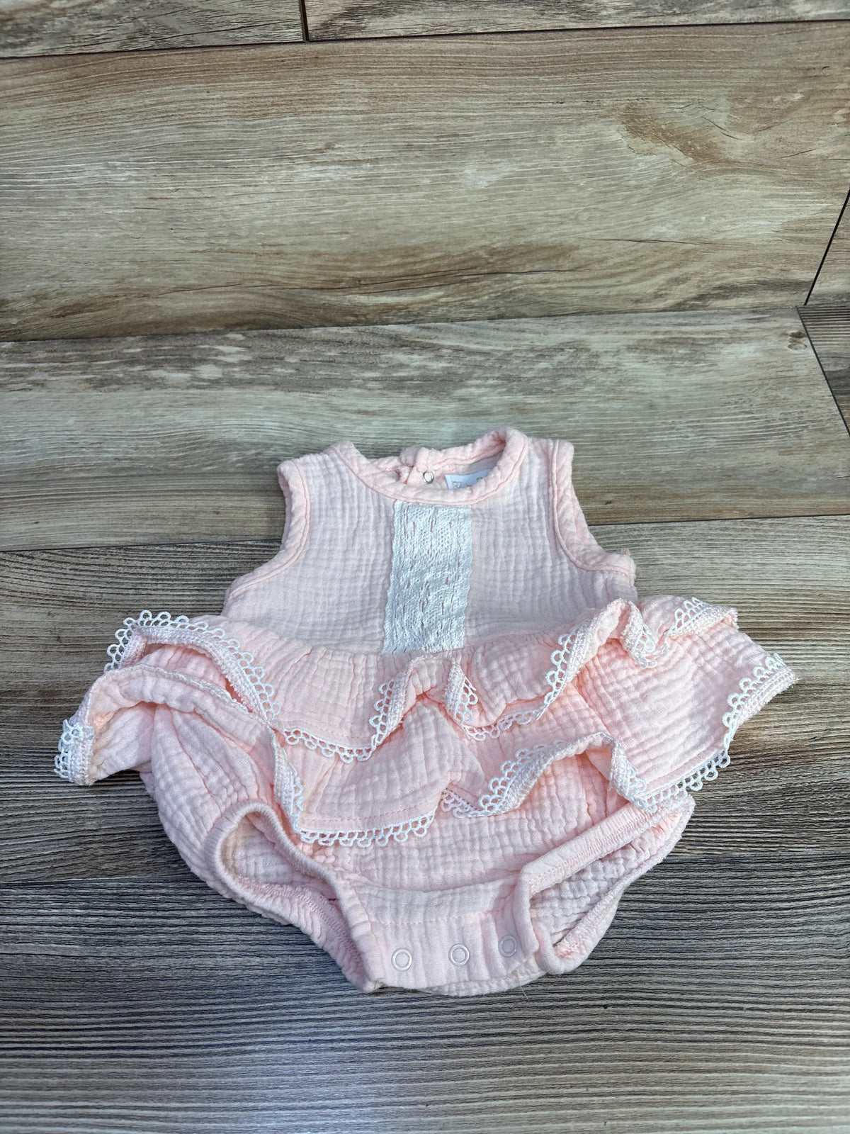 Front view of RZ by Rachel Zoe pink gauze lace bodysuit dress showcasing ruffled lace trim and snap closures on a wood floor