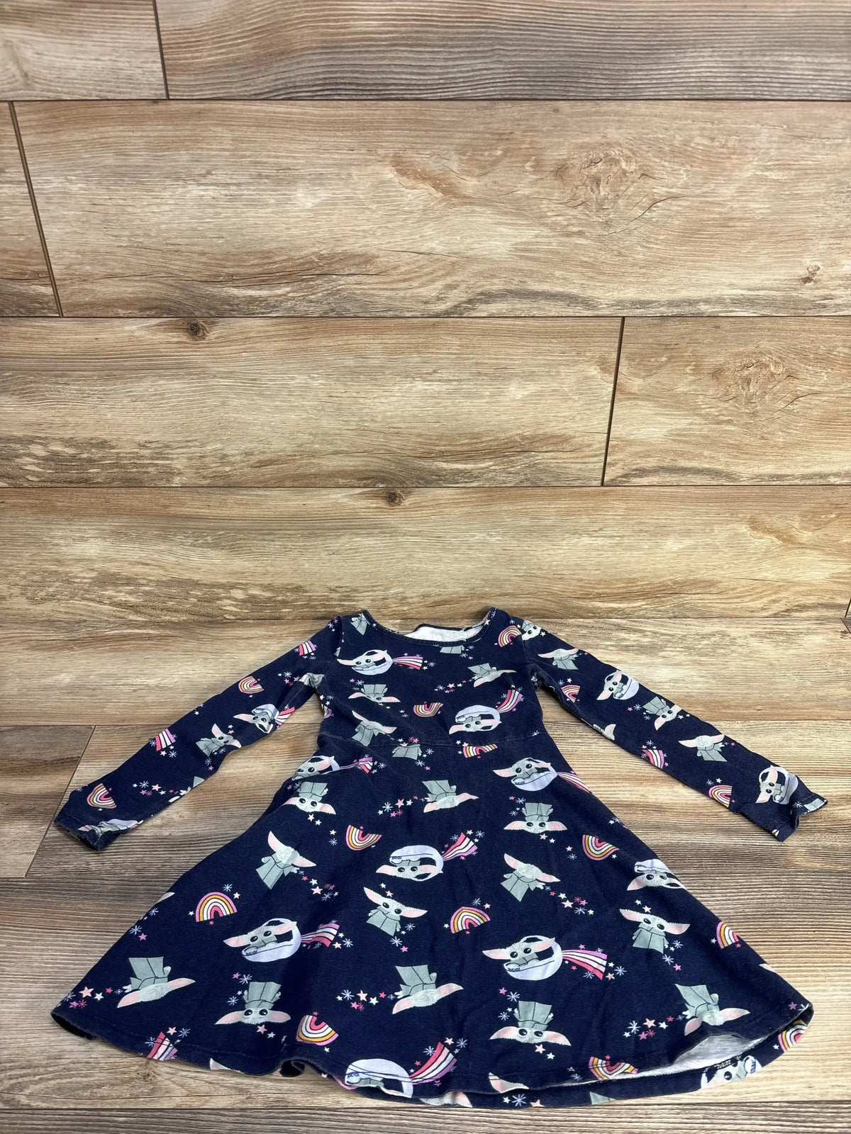 Flat lay of navy Jumping Beans Grogu long sleeve twirl dress with rainbow print on wood floor, size 5T