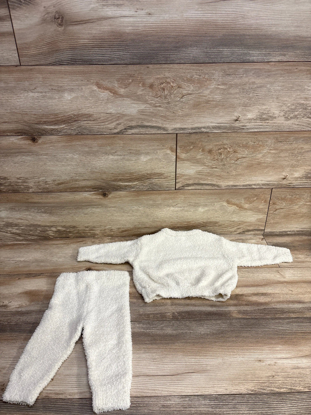 Soft white fuzzy toddler sweater and pants set laid flat on wood floor background