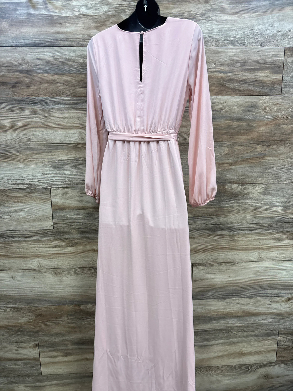 Pink maternity maxi dress with long sleeves and waist tie, displayed on mannequin against wood paneling