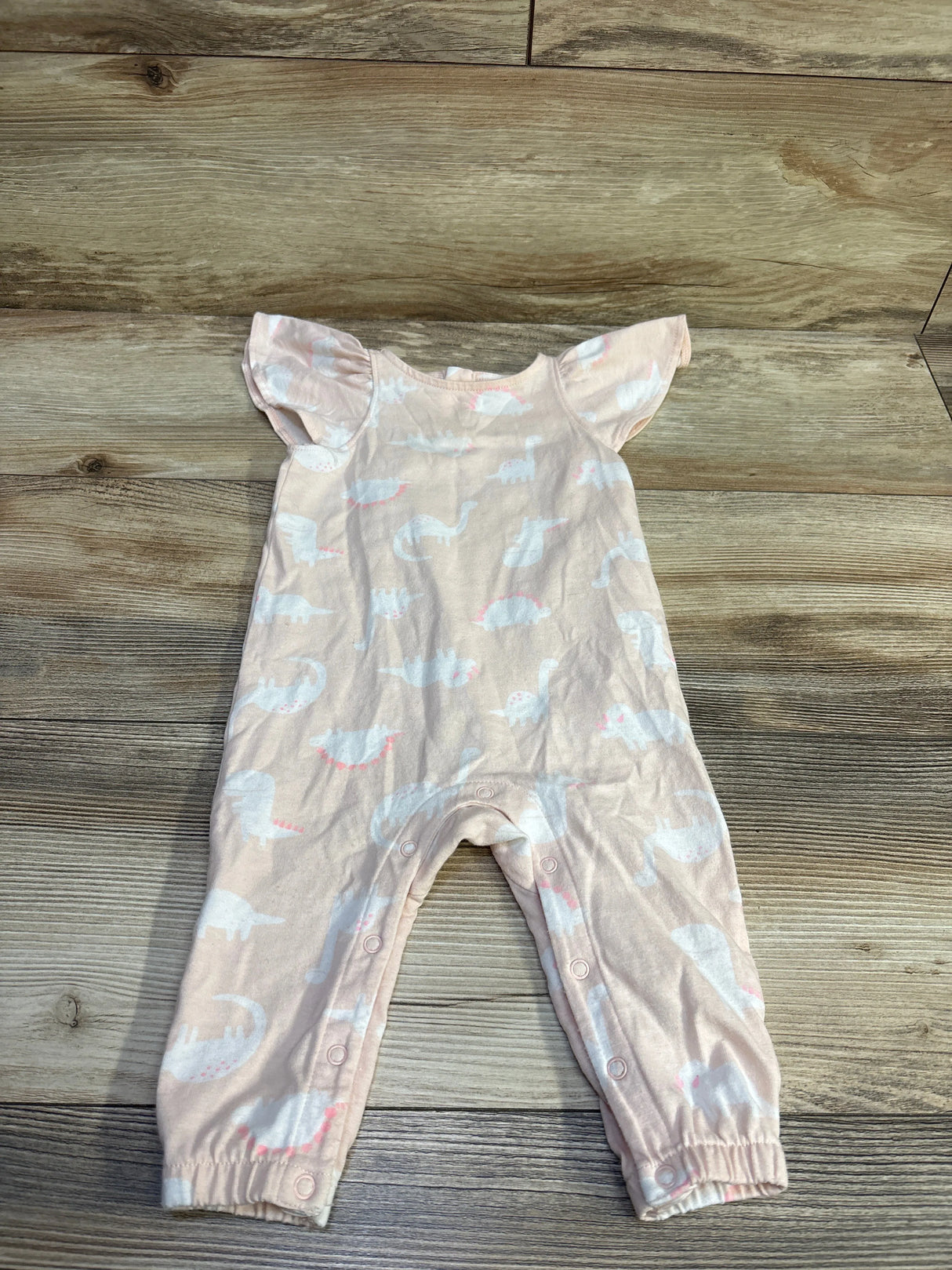 Flat lay of Cat and Jack pink dinosaur-print flutter-sleeve jumpsuit size 3-6M showing snap leg closures on wood