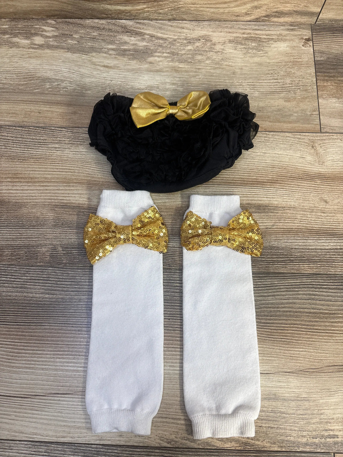 Top view of two piece ruffle bloomers and leg warmers, showing black bloomers and gold bows on white leg warmers