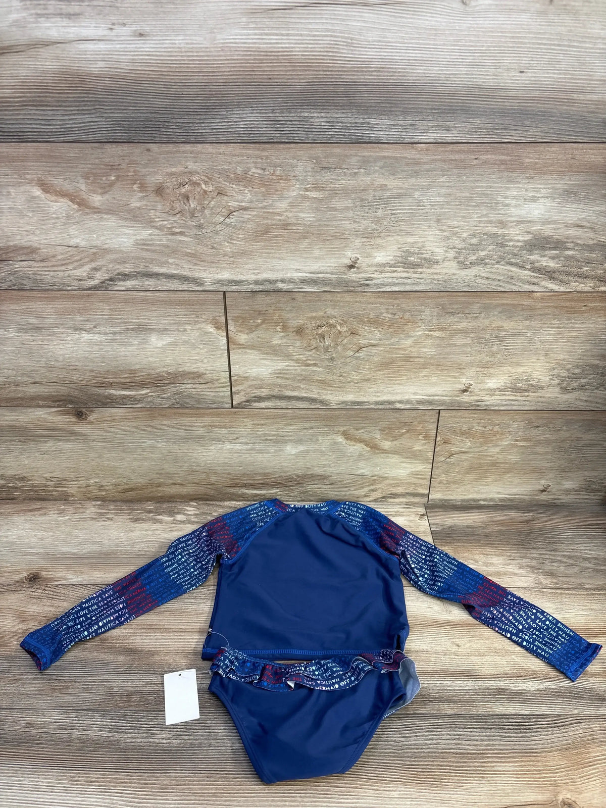 Flat lay of Nautica 2-piece navy rashguard set with printed long sleeves and ruffled bottoms on wood background