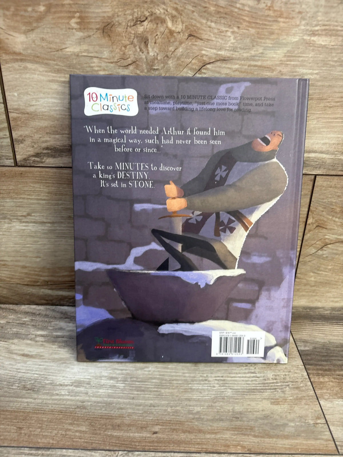 Back cover of King Arthur hardcover book showing an illustrated knight pulling a sword from a stone on a wood surface