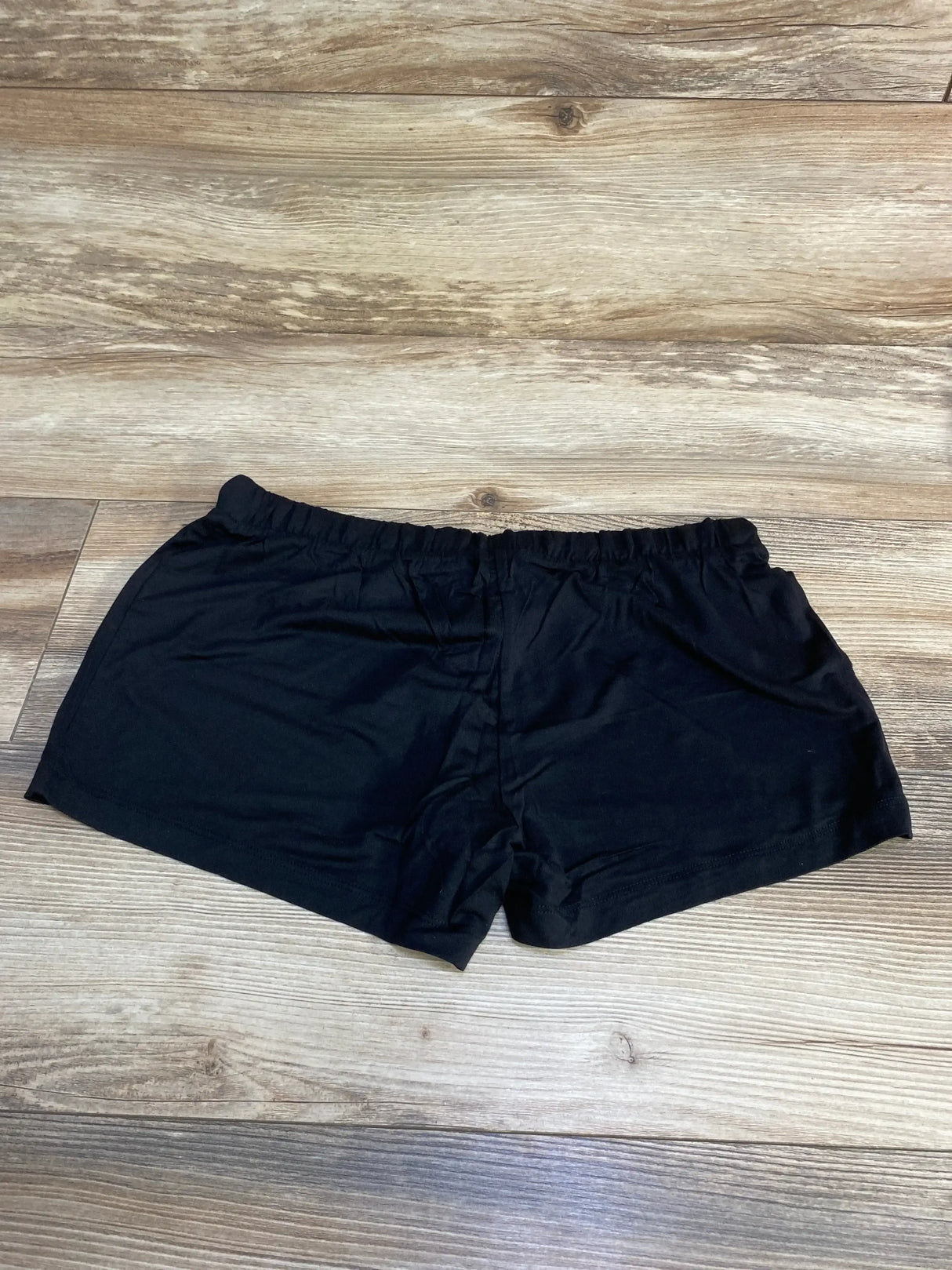 Flat lay of NWOT Gap Maternity black modal shorts sz XXS showcasing elastic drawstring waistband on wood plank floor