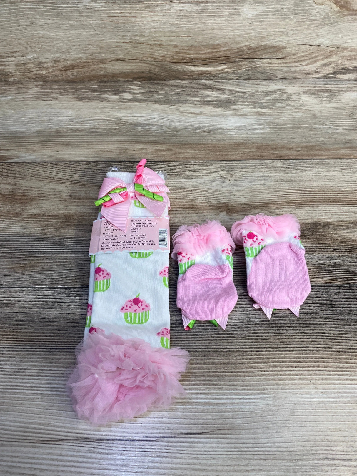 Baby pink cupcake-themed leg warmers and matching socks with frilly tulle accents on wood background