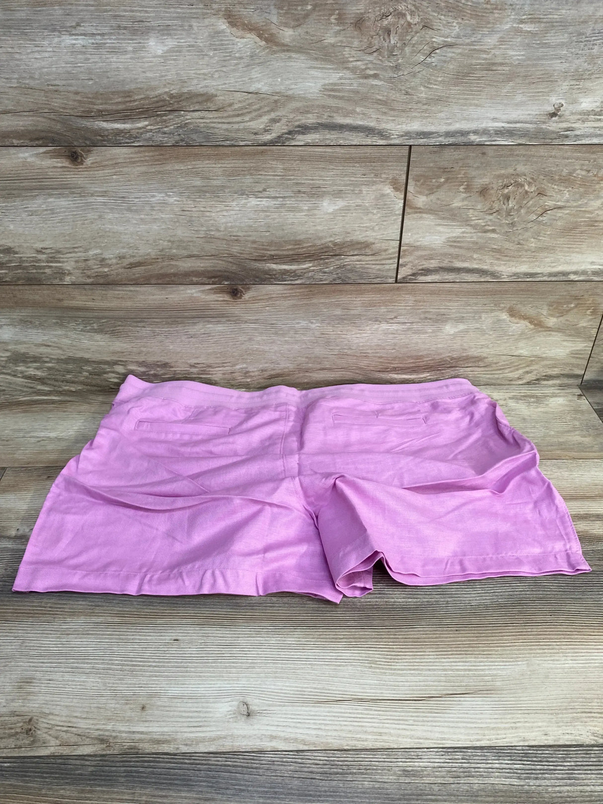 Flat lay back view of pink maternity linen-cotton shorts with back welt pockets and elastic waistband on light wood background