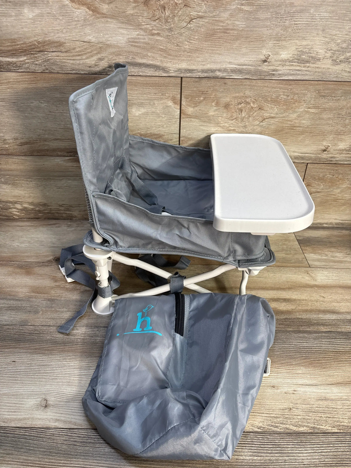 Side view of gray Hiccapop OmniBoost folding booster chair showcasing tray, harness, and carry bag on a wood floor