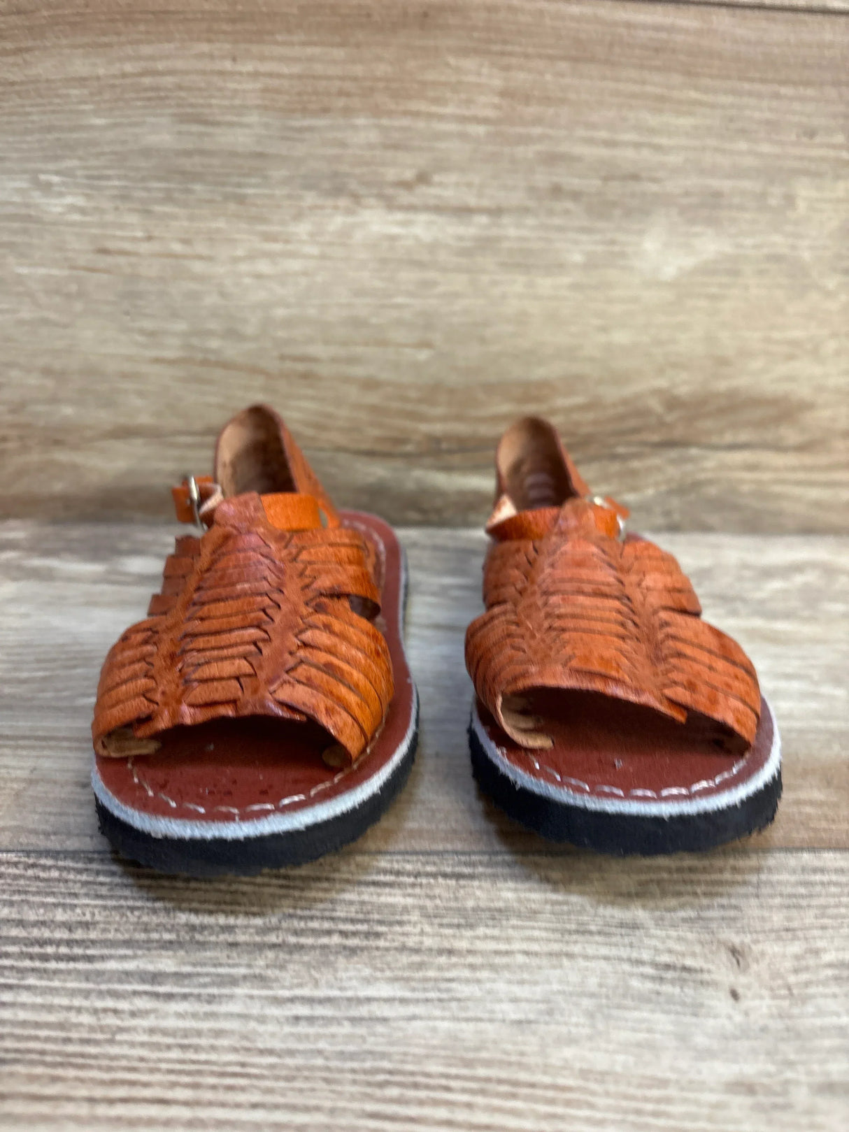 Brown leather kids huarache sandals with woven design on wood background