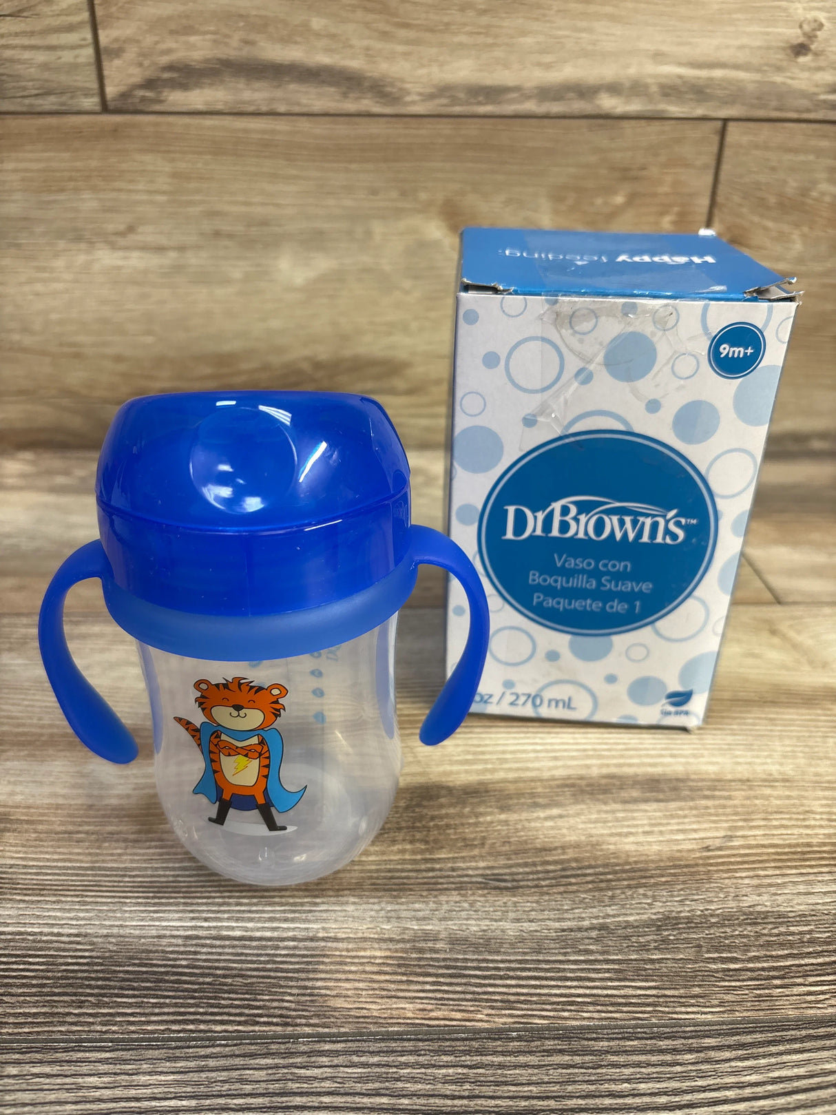 Front view of Dr Brown’s 9 oz soft spout toddler cup showing blue lid and handles, tiger graphic, and box on wooden surface