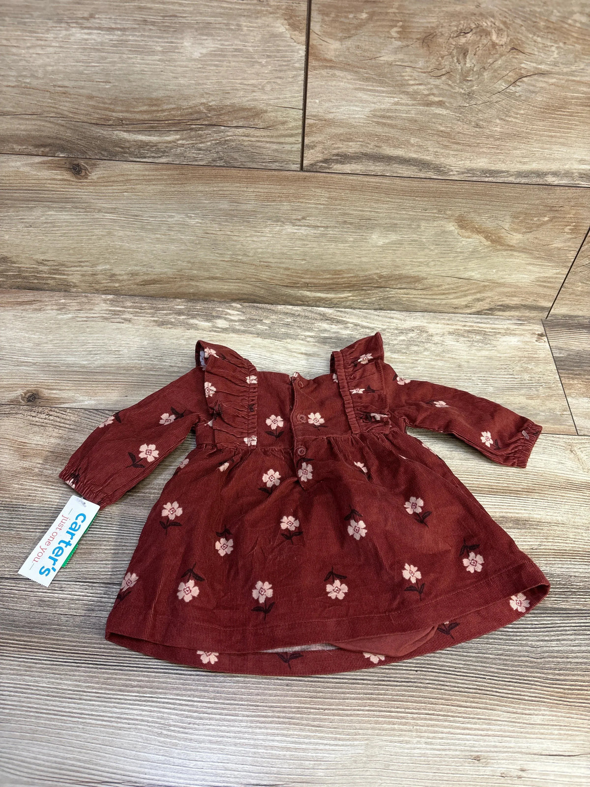 Top-down view of brown corduroy baby dress and bloomers showcasing pink floral print and ruffle shoulders on light wood floor