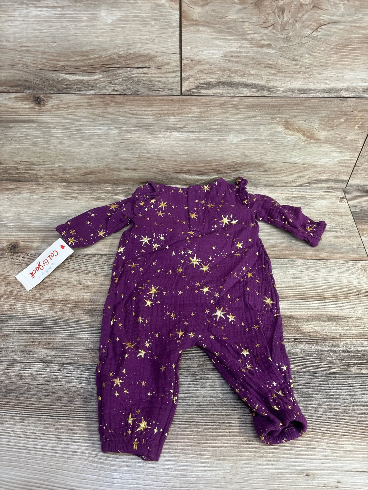 Purple baby romper with gold star pattern, long sleeves, displayed on wood floor
