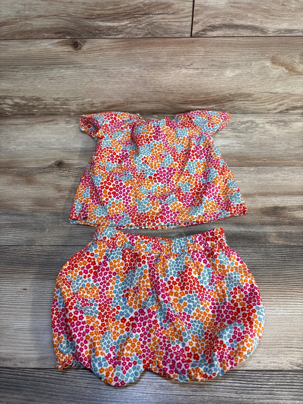 Flat lay of Tucker + Tate colorful floral button blouse and matching bubble shorts, ruffled neckline and elastic waist on wood floor