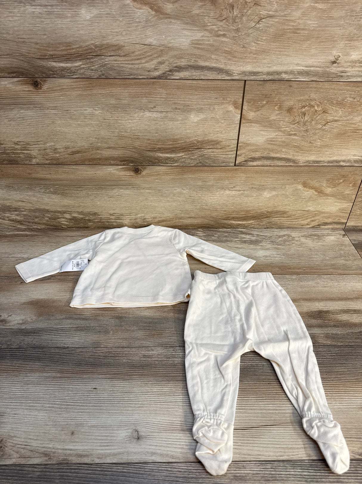 Cream-colored baby outfit with long sleeve top and footed pants on wooden background