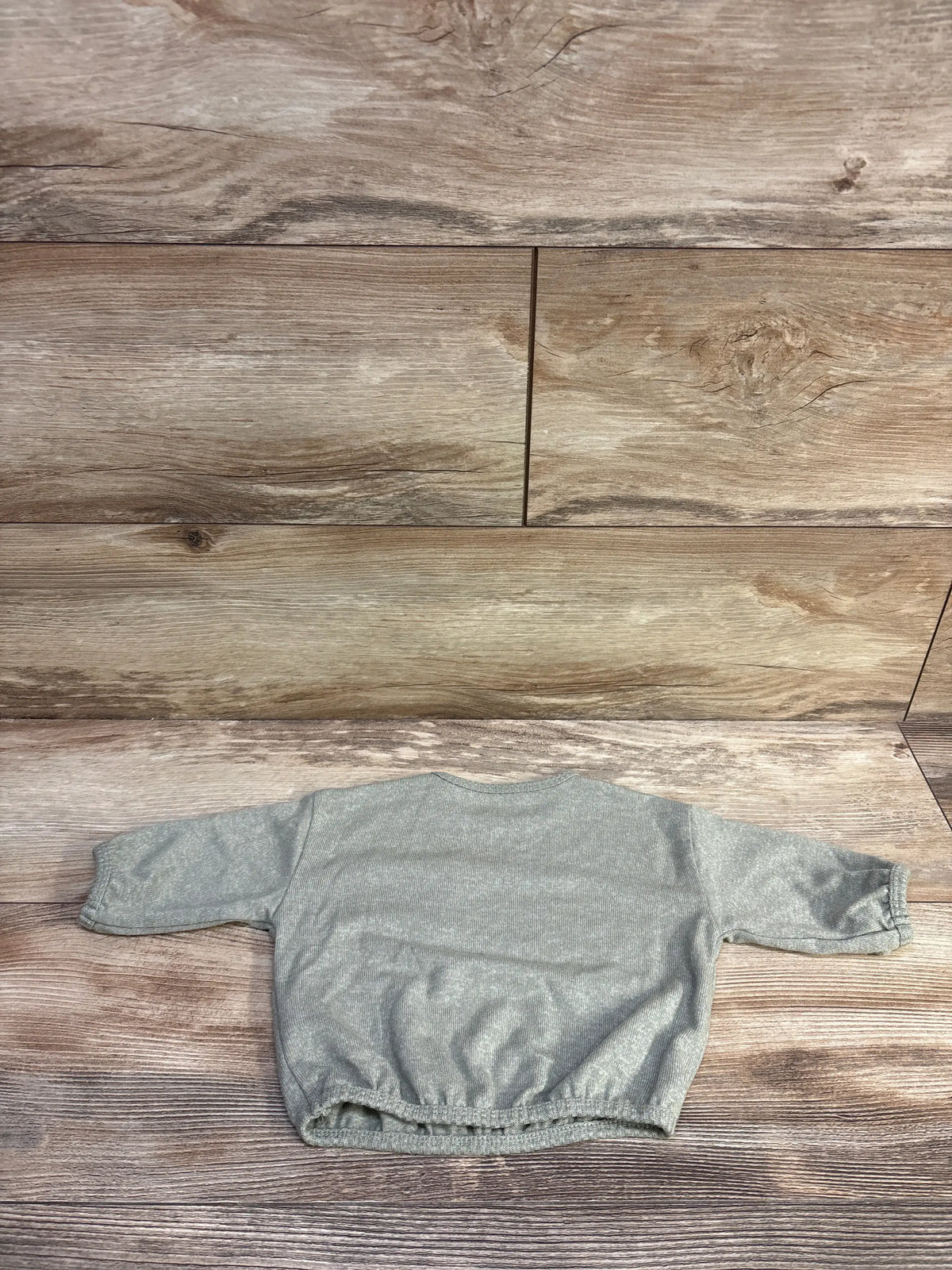 Front view of Easy Peasy long sleeve shirt in soft green with long sleeves and gathered hem on a wood background