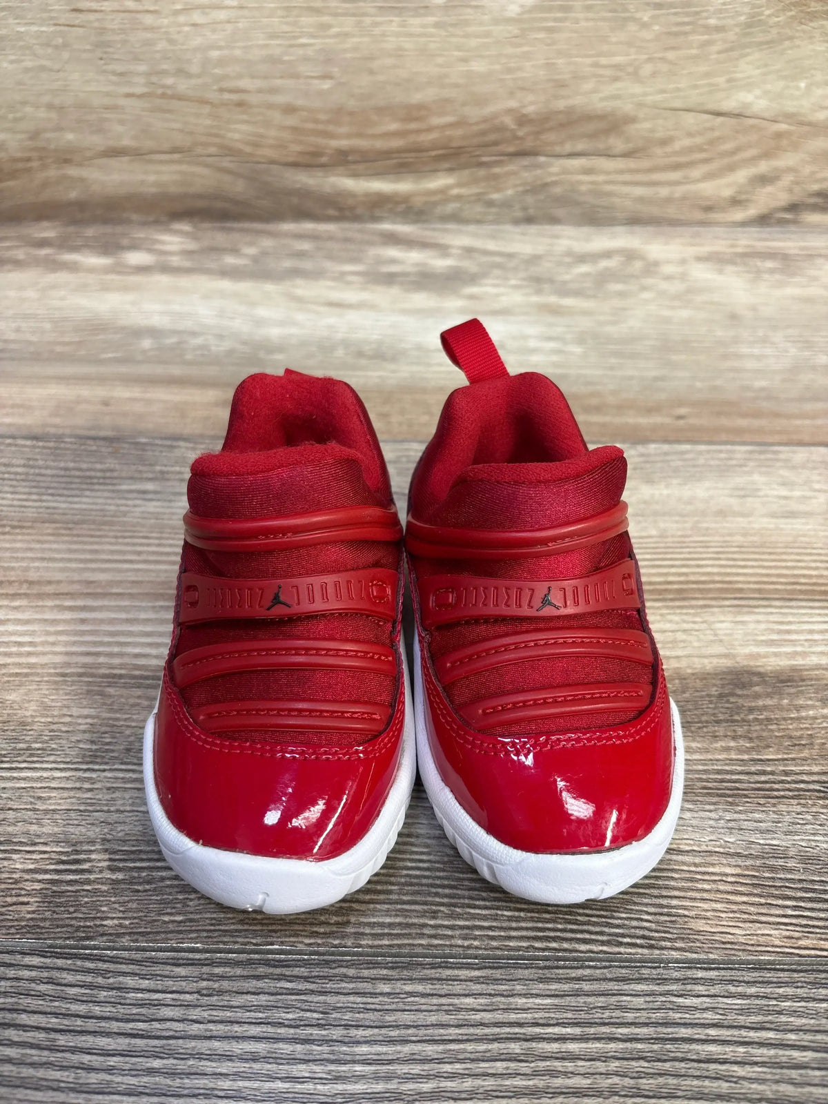 Front view of Air Jordan 11 Retro Little Flex TD ‘Gym Red’ sneakers showcasing slip-on closure and white soles on wood surface