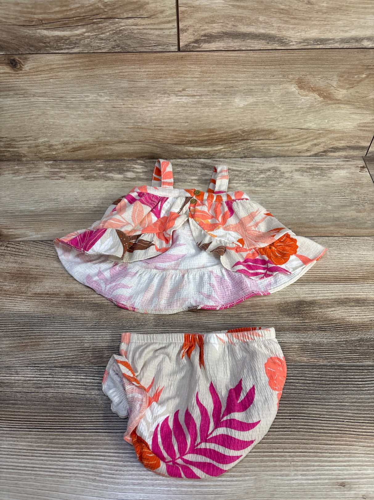 Flat lay of Carter's 2-piece floral tank and bloomers in beige with pink leaf print, ruffle hem and elastic waist on wood