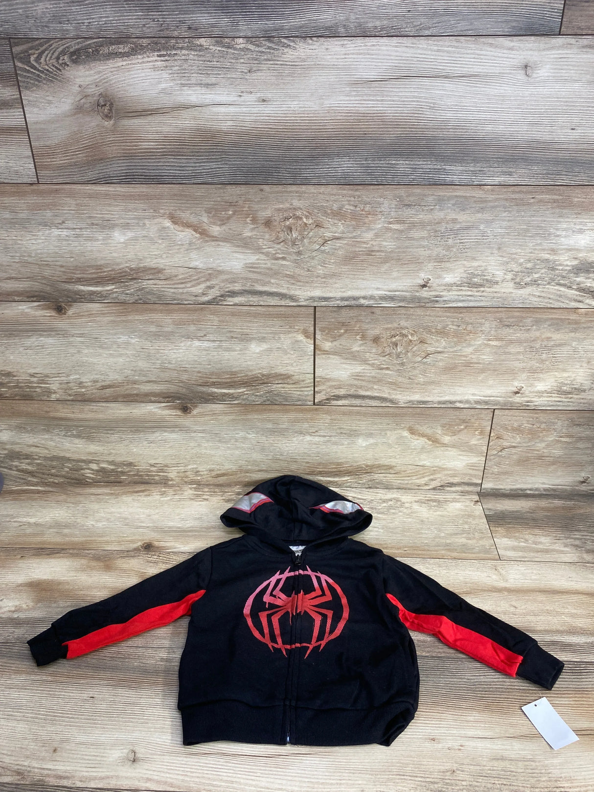 Kids black and red Spiderman hoodie with spider logo, zip-up, laid flat on wooden floor