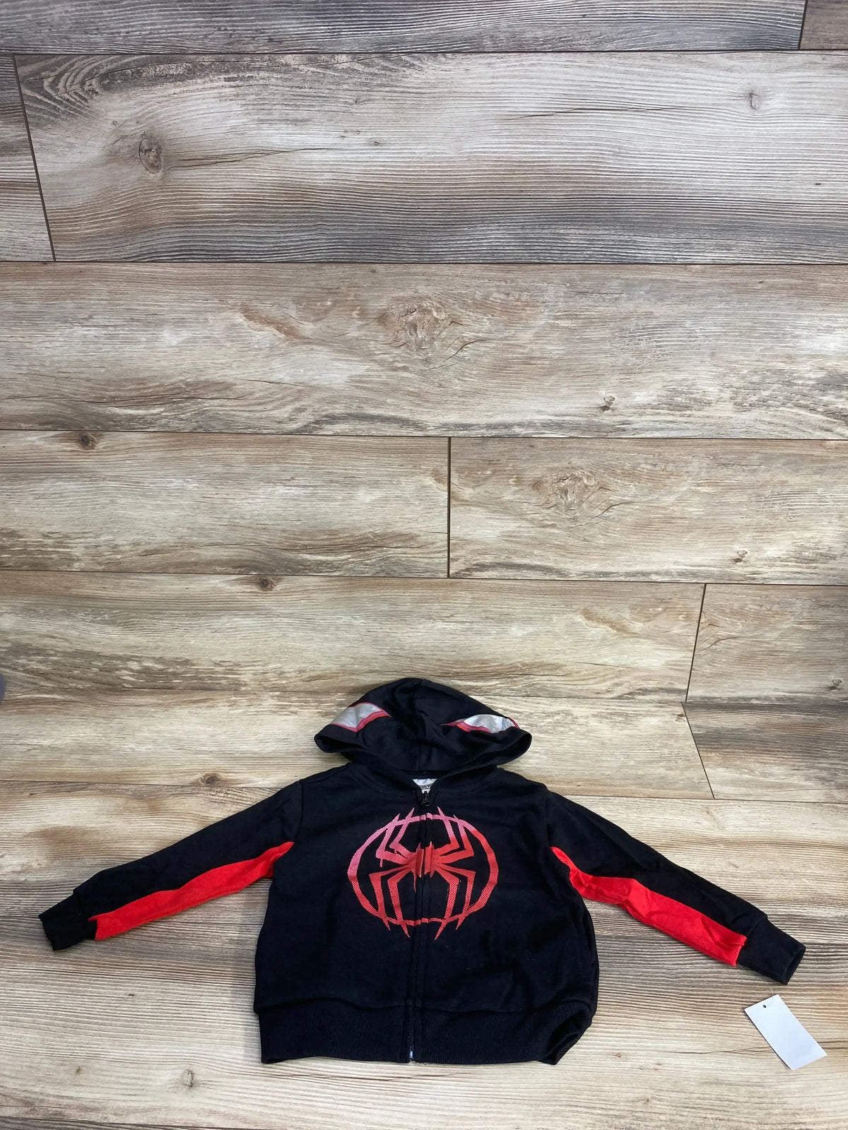 Kids black and red Spiderman hoodie with spider logo, zip-up, laid flat on wooden floor